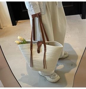 Close-up of straw woven tote with brown leather straps, tassel details and tulip accents