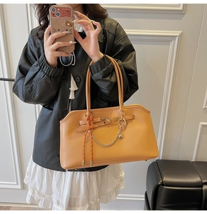 Detail of warm orange-brown leather tote bag with gold chain and woven rope charm