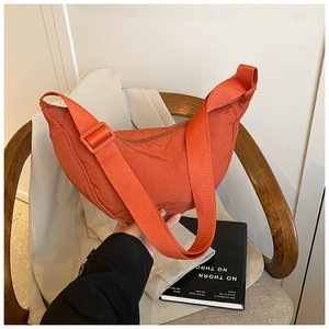 Detail of an orange-red nylon crescent bag with adjustable wide strap on a wooden chair