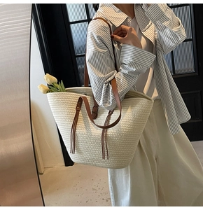 Detail of white straw tote bag featuring brown leather handles and decorative tassel detail
