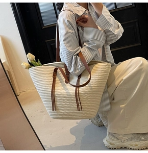 Close-up of a large beige straw tote bag with brown leather straps and elegant tassel