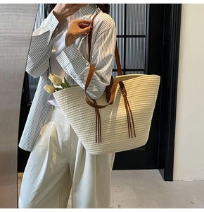 Detail view of woven straw tote bag featuring leather straps and decorative long tassels