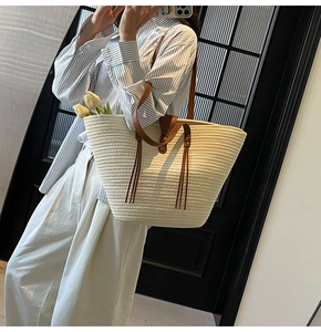 Detail of woven straw tote bag with brown leather straps and decorative fringe tassel