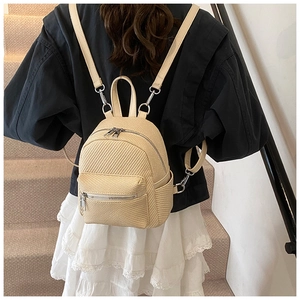 Detail of a beige woven mini backpack with silver zippers worn by a model indoors