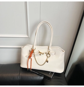 Creamy white shoulder bag featuring gold chain heart charm and orange woven accessory