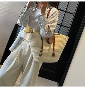 Detail of straw woven tote bag with brown leather straps and bohemian tassel decoration