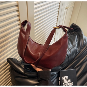 Detail of burgundy crescent bag with smooth leather texture and gold hardware