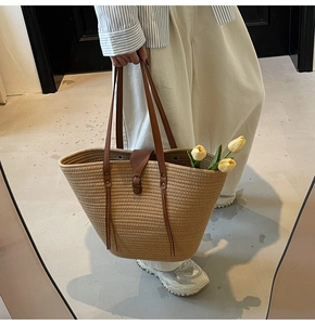 Detail of woven straw tote bag with brown leather handles and decorative buckle strap
