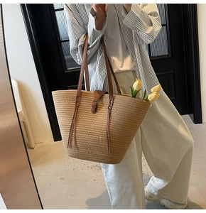 Detail of hand-woven straw tote with leather handles and decorative fringe tassel