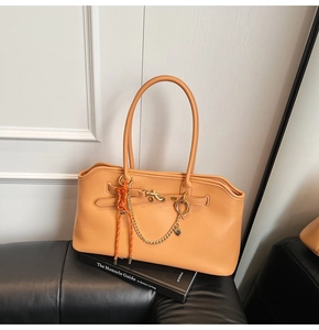 Detail of a bright orange leather tote bag with metallic chain on a black sofa