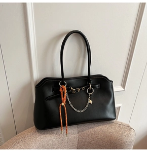Detail of black tote bag with gold chain and orange lanyard on a textured chair
