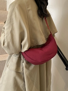 Minimalist burgundy nylon crescent shoulder bag shown on model with trench coat