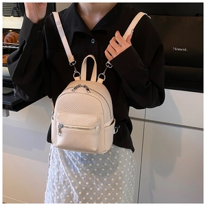 Close-up of a cream woven mini backpack shown on a model in a casual indoor setting