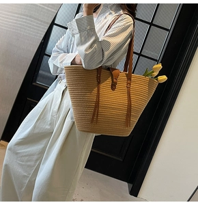 Detail of woven straw tote bag with brown leather straps and long decorative tassels
