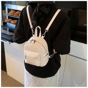 Close-up of beige quilted mini backpack on female model in a modern bakery setting