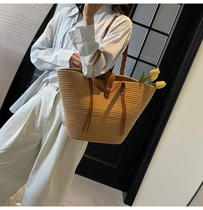 Detail view of woven straw tote bag featuring brown leather straps and elegant fringe decor