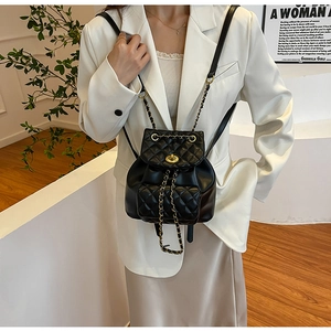 Détail d'un mini sac à dos noir matelassé avec chaîne dorée porté par un mannequin