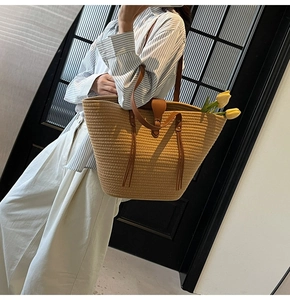Detail of large woven straw tote bag with brown leather tassels and shoulder straps