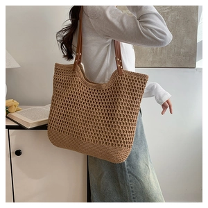 Detail of hollow woven tote bag featuring brown leather straps and silver metal rivets
