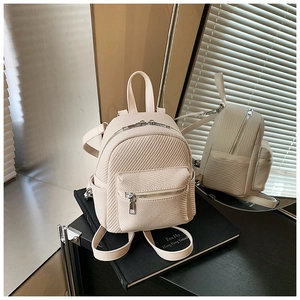 Detail of beige mini backpack with woven texture and silver zippers on a book stand
