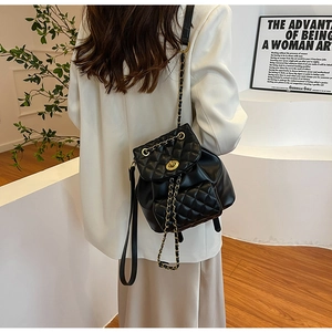 Détail d'un sac à dos en cuir matelassé noir avec chaîne dorée et fermoir pivotant sur modèle