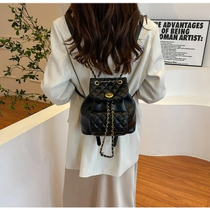 Détail d'un sac à dos en cuir noir matelassé avec chaîne dorée et fermoir tournant sur un mannequin