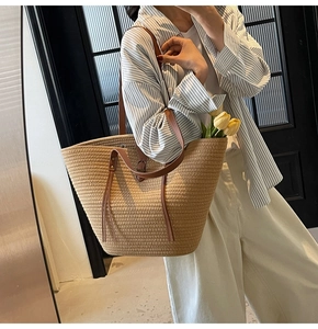 Detail of straw woven tote bag featuring brown leather straps and decorative tassel
