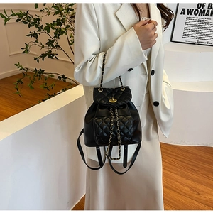 Détail d'un mini sac à dos noir matelassé avec chaînes dorées porté par un mannequin