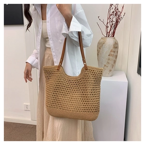 Detail of woven straw shoulder bag with hollow design and brown leather handle