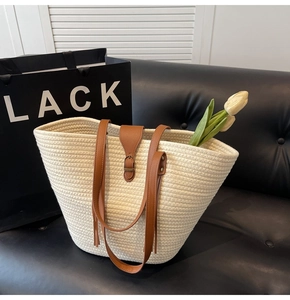 Detail shot of woven straw tote bag with brown leather straps and metallic buckle on black sofa