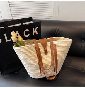 Detail of woven straw tote bag with brown leather handles and decorative buckle on a sofa