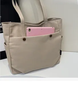 Detail view of canvas tote bag showing front pocket with dark buttons and side logo