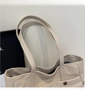 Detail of beige canvas tote bag showing durable shoulder strap and outer pocket with button