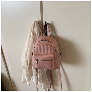Detail of light pink mini backpack with fine woven texture hanging on a white door hook
