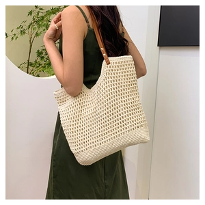 Close-up of beige hollow-out woven tote bag with brown leather straps and metal rivets