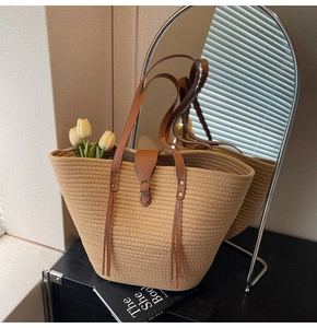 Detail of hand-woven straw tote bag with brown leather handles and decorative tassel