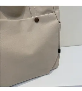 Detail of beige canvas tote bag showing high-density texture, snap button and side pocket