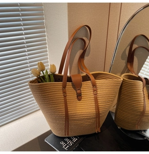 Detail of straw woven tote bag featuring brown leather buckle and long fringe tassels