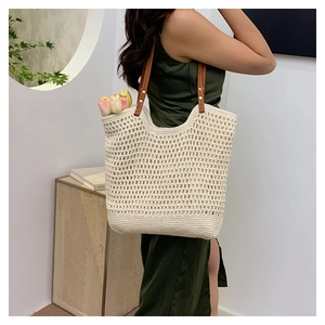 Detail of hollow-out mesh straw tote with brown leather handle and metal rivet accents