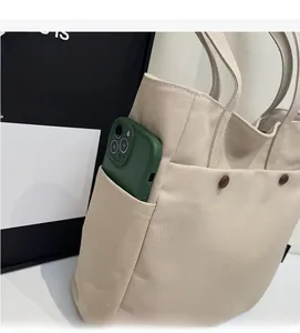 Detail view of large front pocket on beige canvas tote bag with a smartphone inside