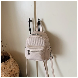 Detail view of woven texture and silver zipper on a beige mini backpack in home setting