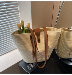 Detailed macro view of woven straw tote bag with brown leather straps and tassels