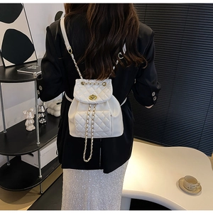 Détail de dos d'un sac à dos en cuir blanc matelassé avec chaîne dorée et fermoir pivotant
