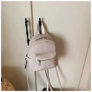 Detail of beige mini backpack with woven texture hanging on a vintage door handle