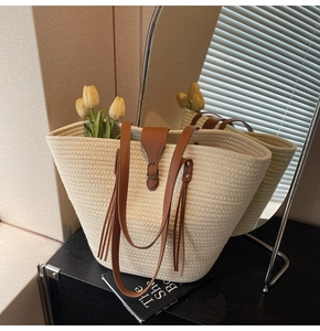 Close-up of woven straw tote bag featuring brown leather straps and elegant tassel detail