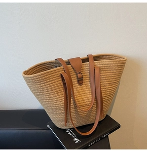 Detail of woven straw tote bag featuring brown leather straps and stylish tassel charm