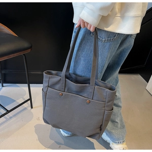 Detail of dark grey canvas tote bag featuring front pockets and bronze metal buttons