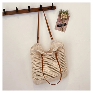 Detail of hollow-out woven tote bag featuring brown leather handles with metal rivets