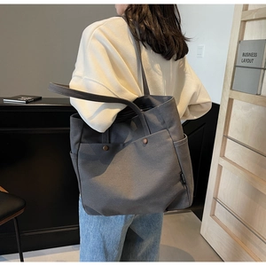 Detail of dark gray canvas tote bag with brown button pockets shown on model's shoulder