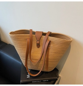 Detail of woven straw tote bag featuring brown leather shoulder straps and flap closure